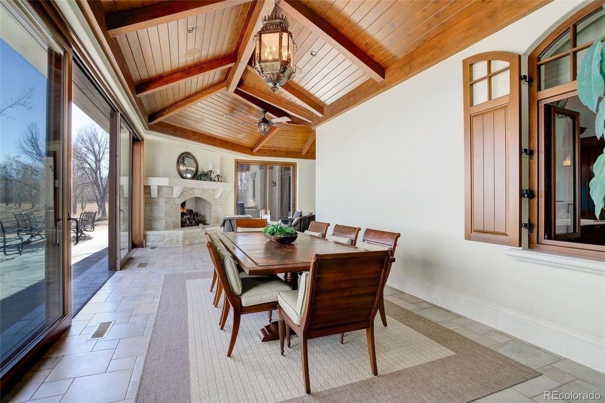 Architectural details such as a coffered ceiling and a stone fireplace add character and charm to this outdoor dining space. The combination of comfortable seating and a large dining table creates a functional and inviting area for al fresco dining.