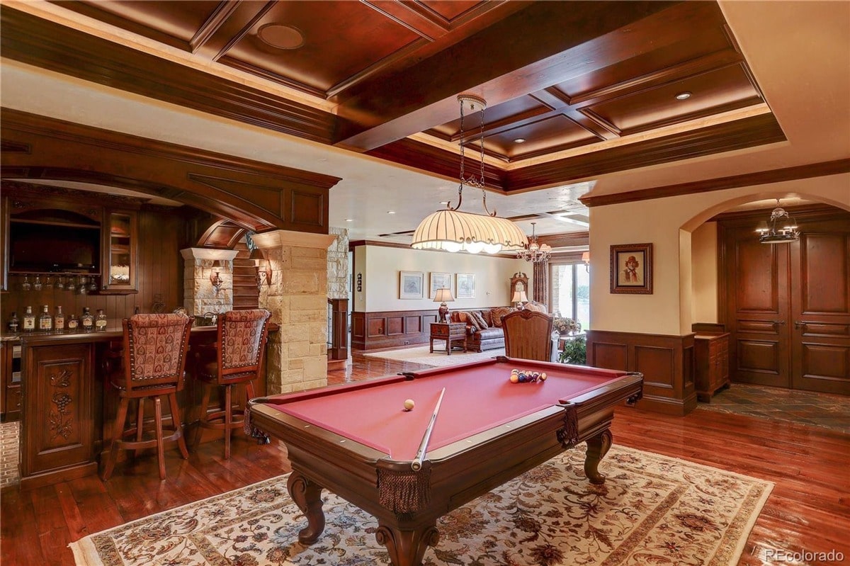 Classic design elements such as rich wood paneling and a coffered ceiling add to the grandeur of this game room. The combination of a pool table and a wet bar creates a space that is both elegant and functional for entertaining.