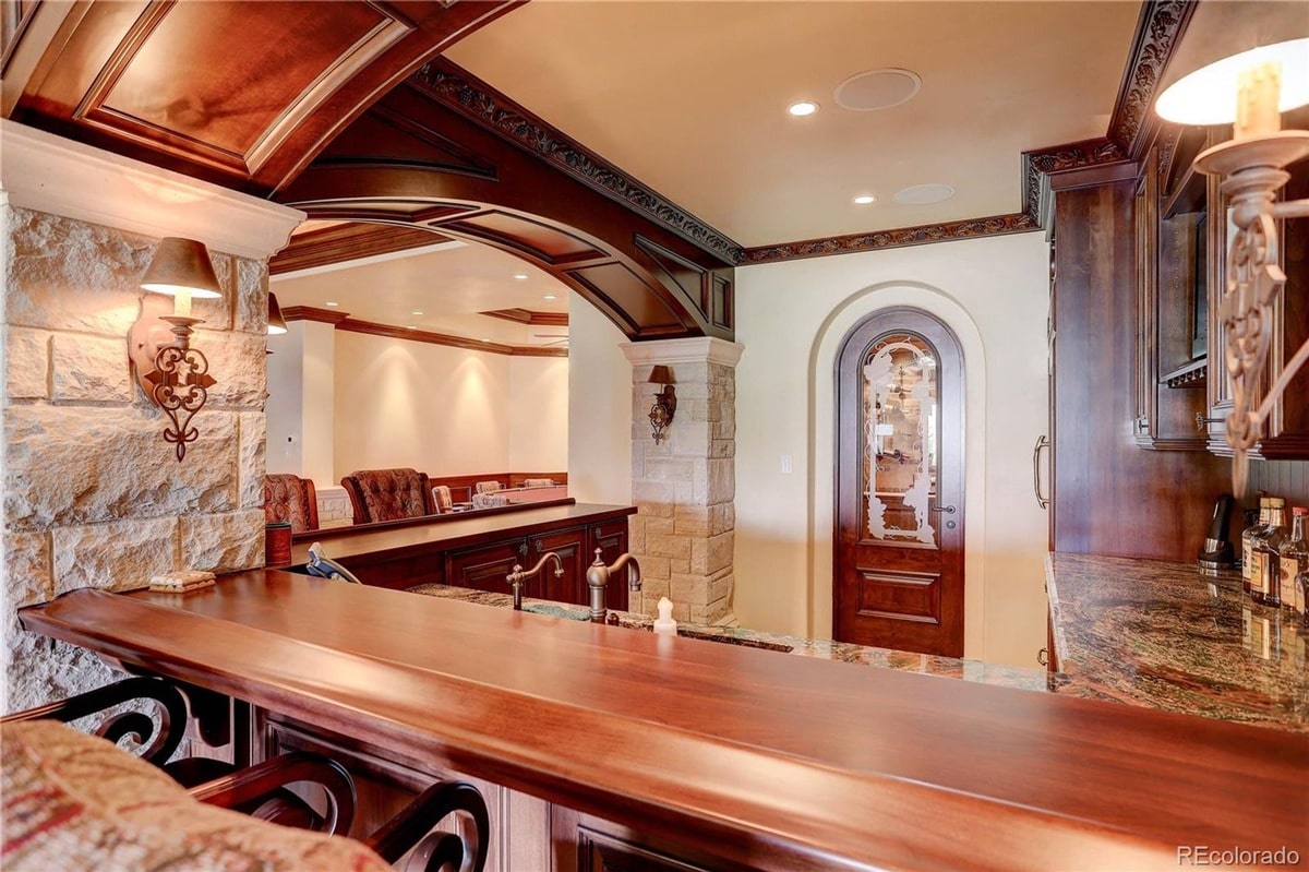 This sophisticated basement bar offers a luxurious and inviting space for entertaining, featuring rich wood finishes and elegant architectural details. The room's warm lighting and comfortable seating create a sophisticated and relaxed atmosphere.