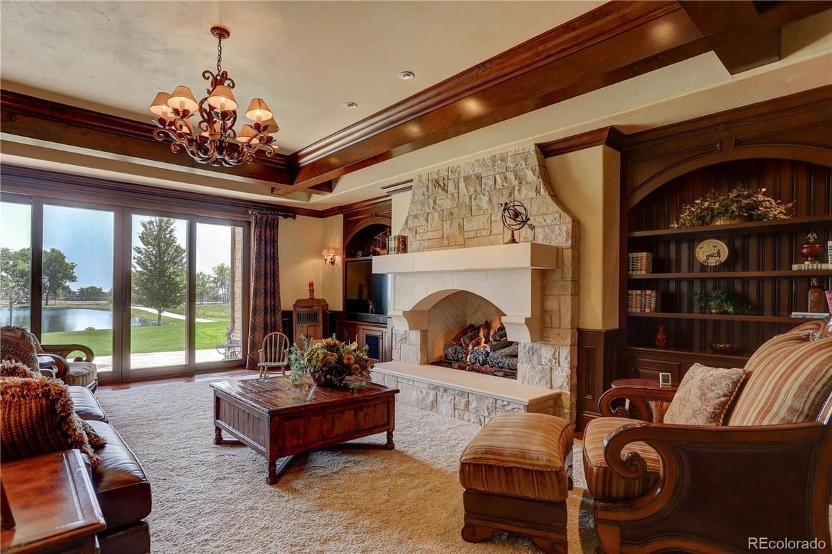 This inviting living room offers breathtaking views of a serene landscape visible through expansive windows. The room's warm and inviting atmosphere is enhanced by a stone fireplace and rich wood accents.