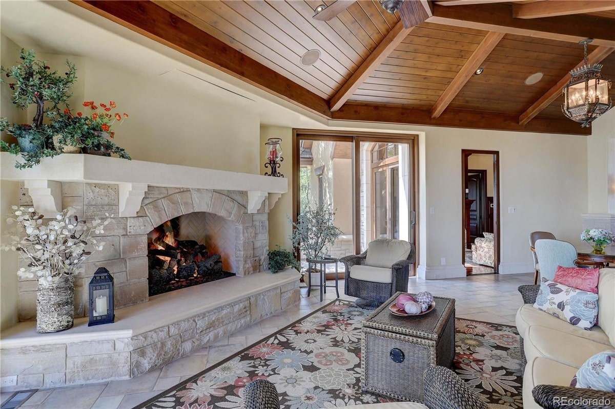 This sun-drenched sunroom exudes relaxed elegance with its stone fireplace, wood-beamed ceiling, and comfortable seating. The room's inviting atmosphere and access to outdoor spaces create a perfect spot for relaxation and entertaining.