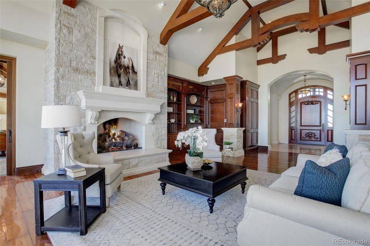 A striking equestrian-themed artwork above the fireplace anchors this elegant living room, setting a sophisticated tone. The room's rich wood beams and expansive windows create a luxurious and welcoming atmosphere.