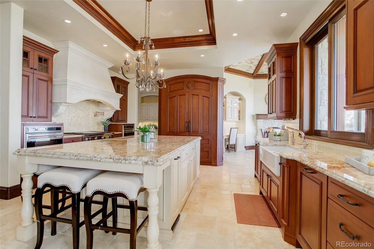 This gourmet kitchen is a masterpiece of design, showcasing luxurious details such as a large granite island and custom cabinetry. The warm color palette and elegant chandelier create a sophisticated and inviting atmosphere.