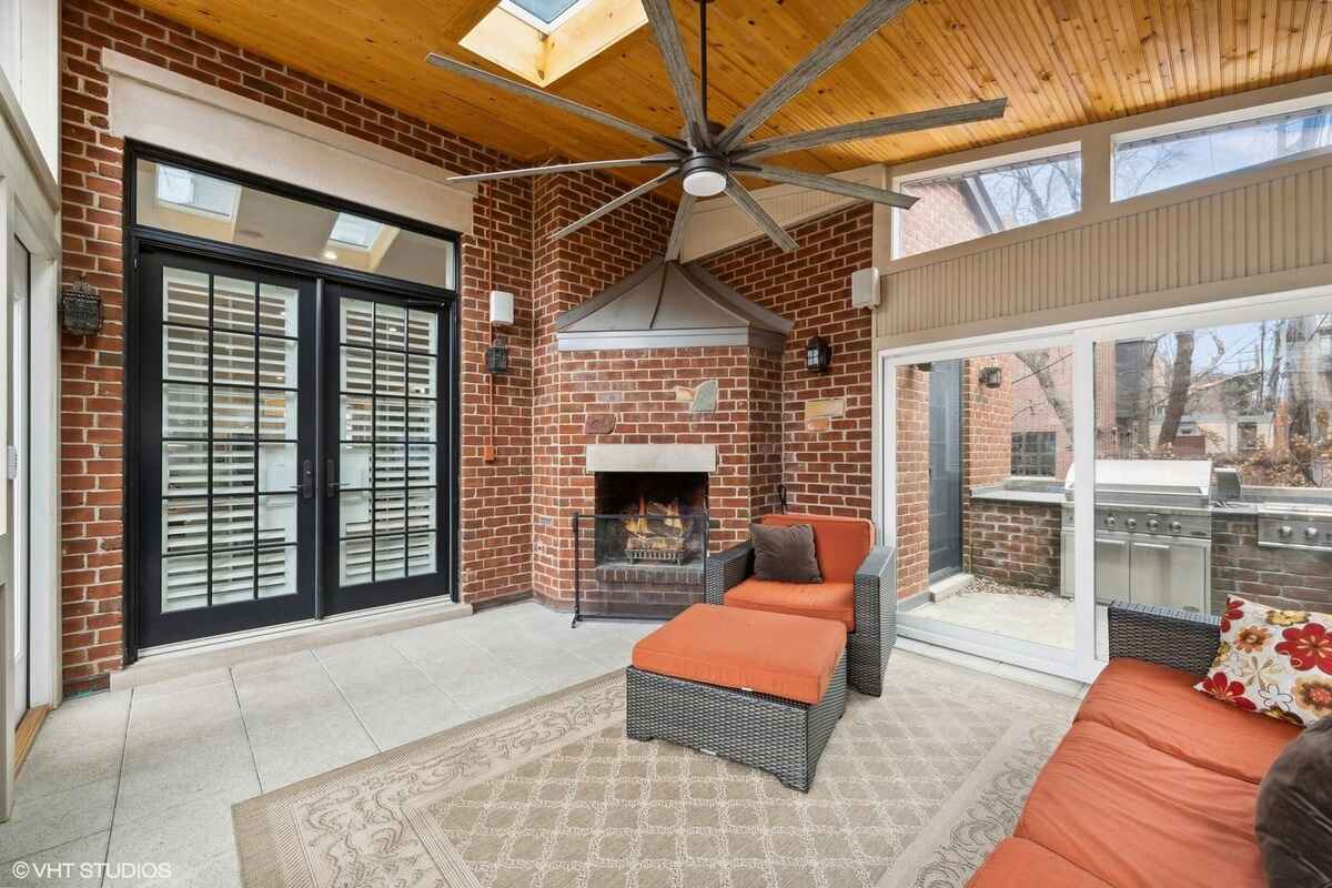 Sunroom with brick walls, a fireplace, a wicker seating set with orange cushions, a large ceiling fan, and sliding doors leading outside.