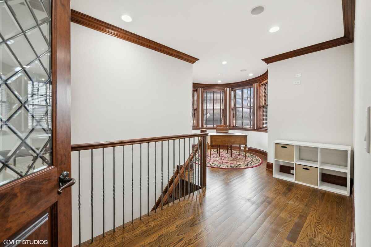 Upper-level landing area has hardwood flooring, decorative wooden trim, and a bay window with a small table and chairs near a storage shelf.