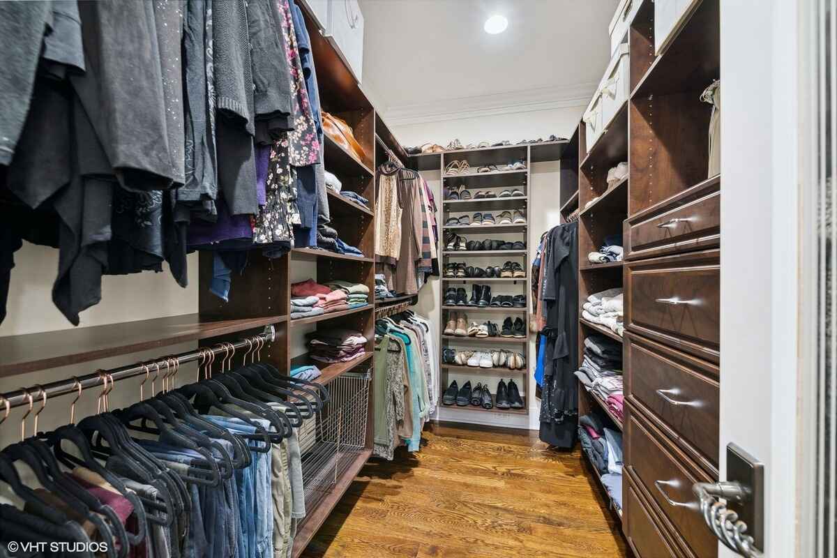 Walk-in closet features hardwood flooring, built-in dark wood shelving, multiple hanging rods, and organized shoe racks.