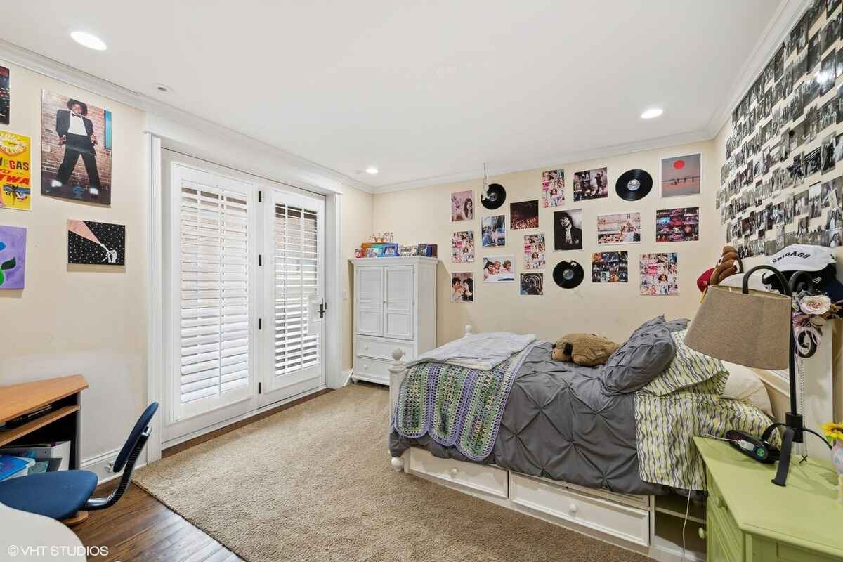 Bedroom includes a white bed frame with built-in storage, a gray and green bedding set, a white wardrobe, a desk, and walls decorated with posters, photos, and vinyl records.