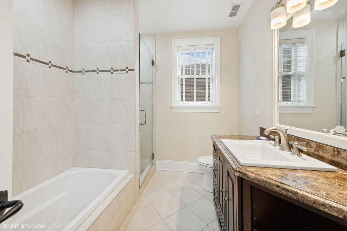 Bathroom includes a tiled shower and tub area, a dark wood vanity with a marble countertop, and a large mirror.