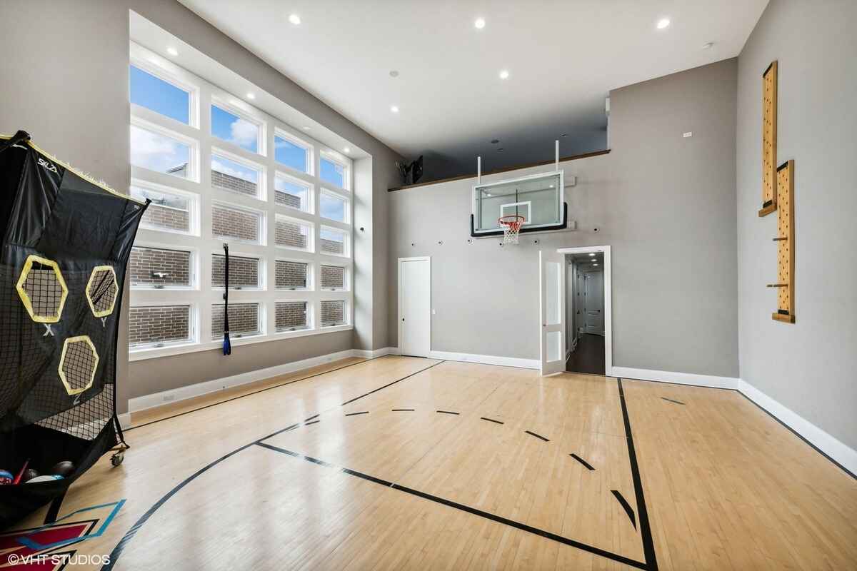 Indoor basketball court features a hardwood floor, a mounted hoop, and tall windows providing natural light.