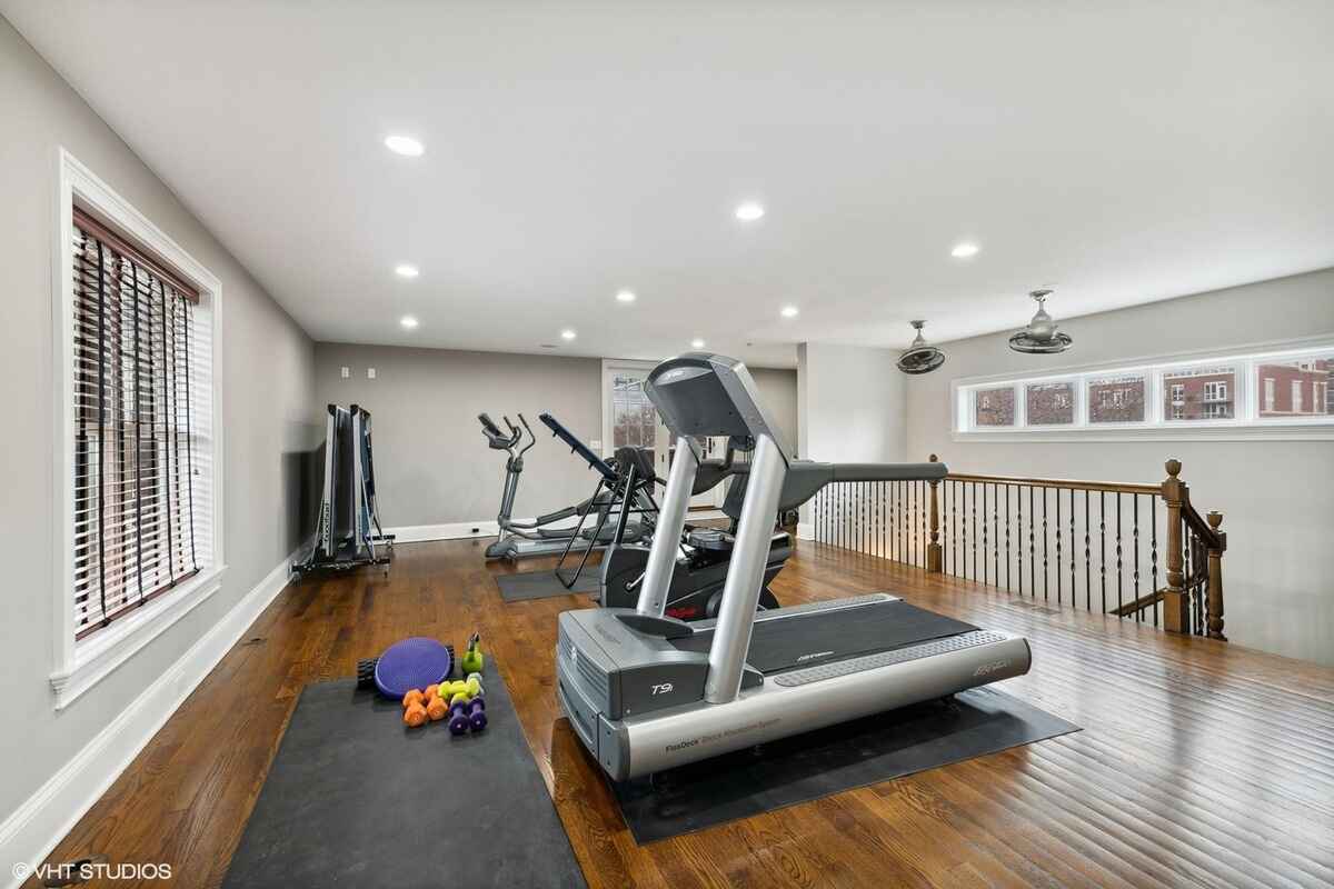 Home gym includes cardio equipment, free weights, and hardwood flooring with natural light from long windows.