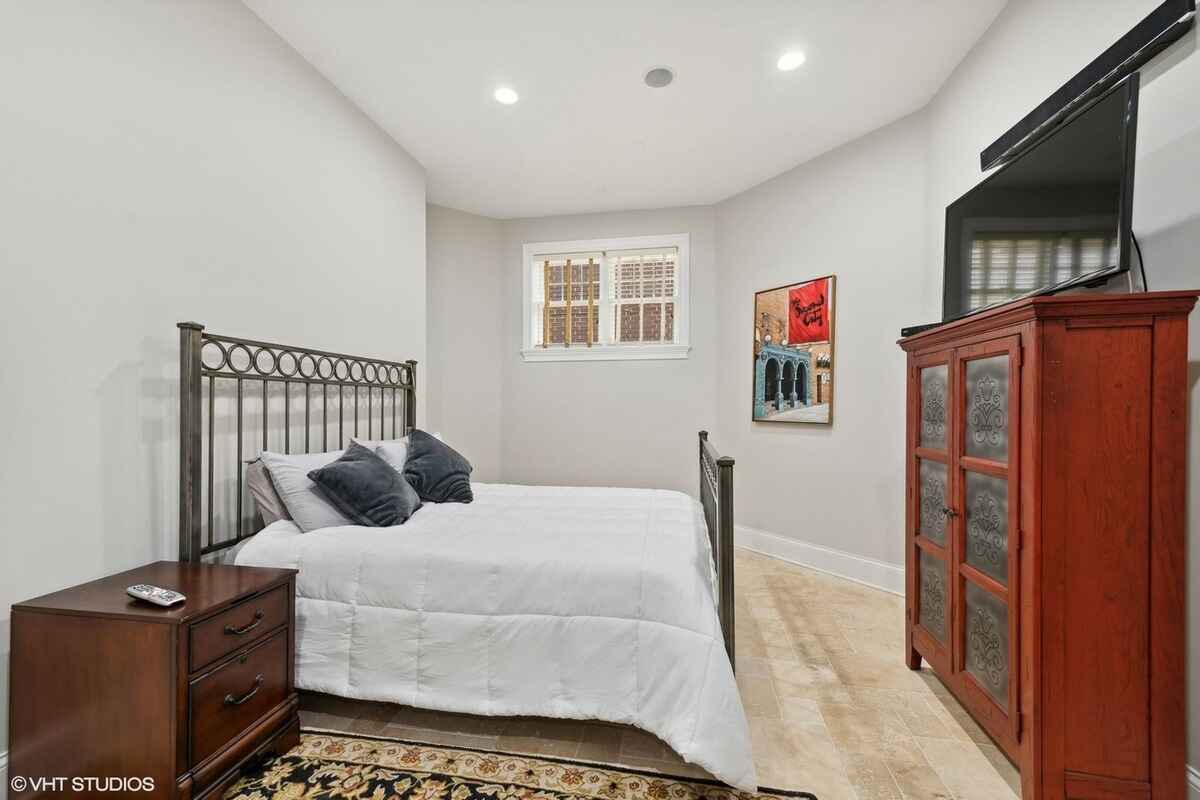 Guest bedroom includes a metal bed frame, a wooden nightstand, a decorative armoire, and tiled flooring.