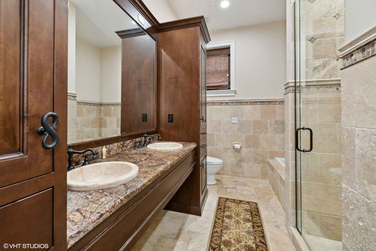 Bathroom features a double sink vanity with a marble countertop, a glass-enclosed shower, and tiled walls and flooring.