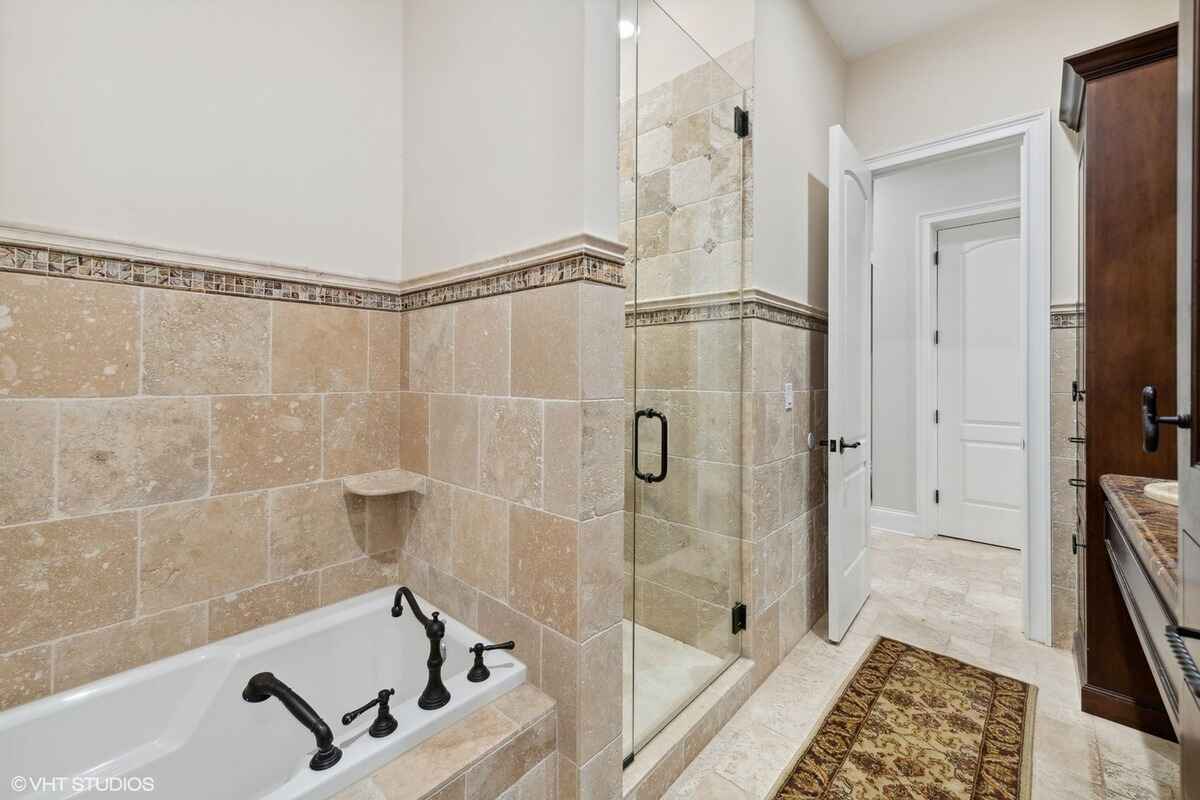 Tub area is accented with tiled walls, dark metal fixtures, and a separate glass shower.