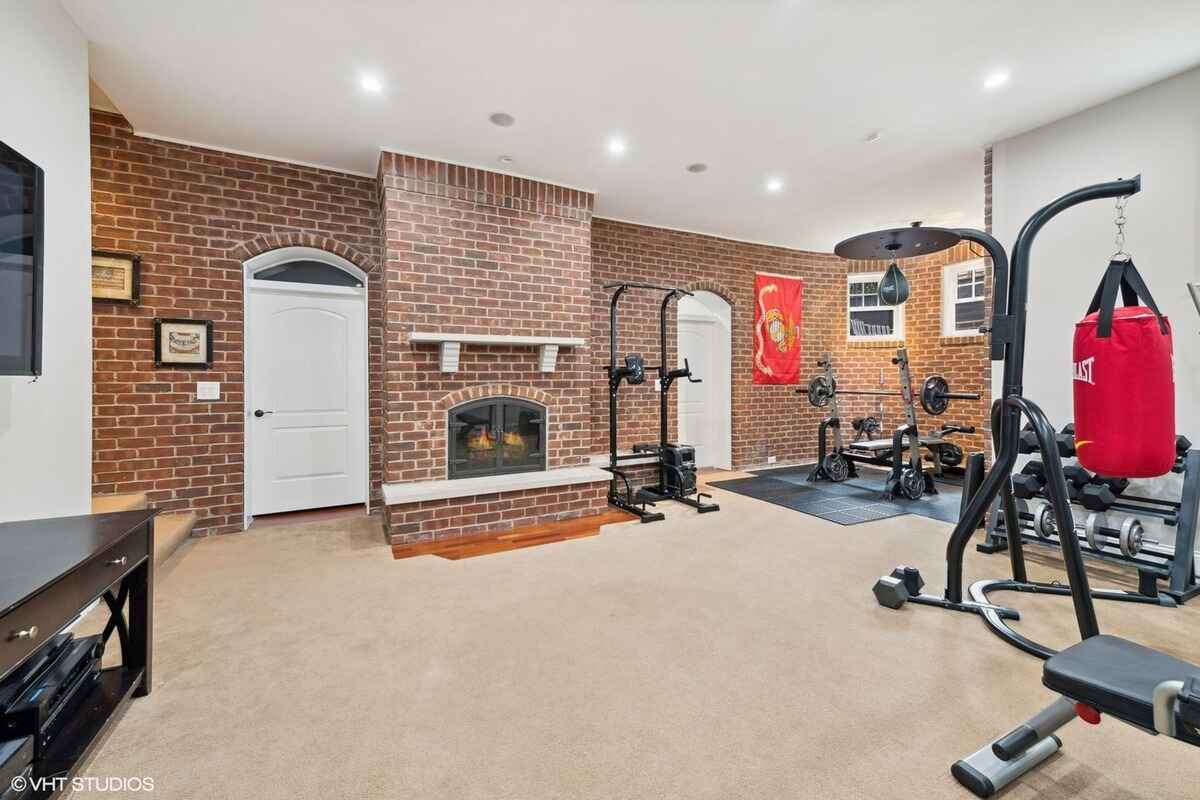 Home gym includes a fireplace with a brick accent wall, workout equipment, and carpeted flooring.