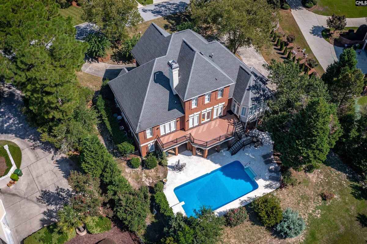 Aerial view of a brick home with a swimming pool surrounded by greenery.