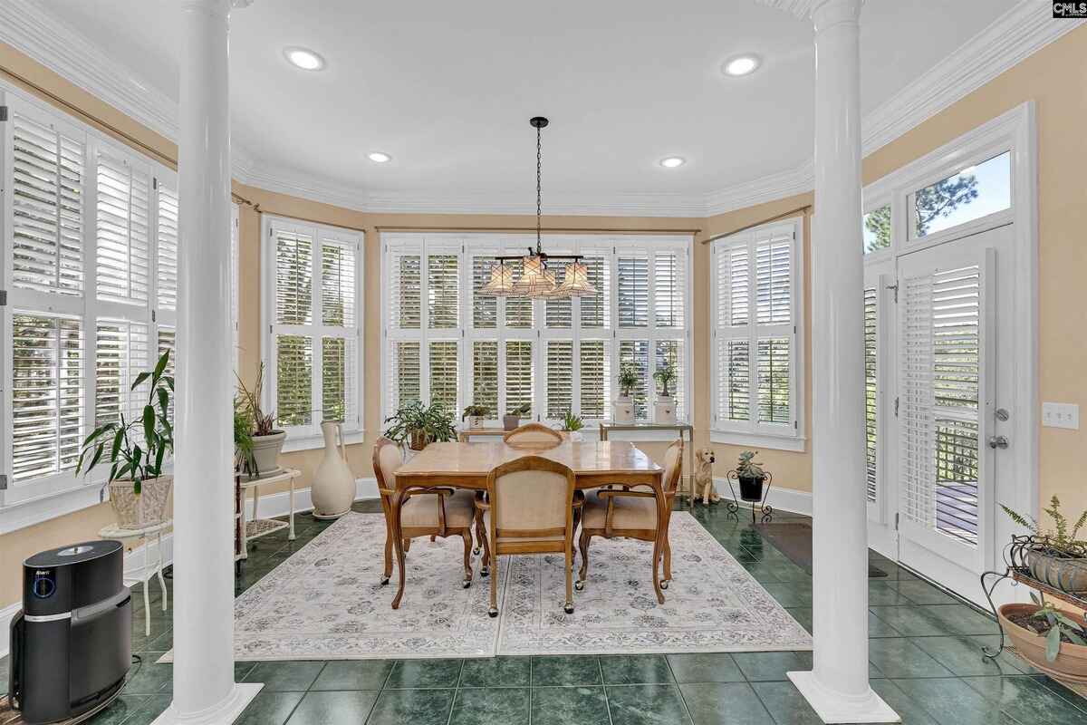 Dining room highlights a chandelier, columns, and an abundance of natural light from surrounding windows.