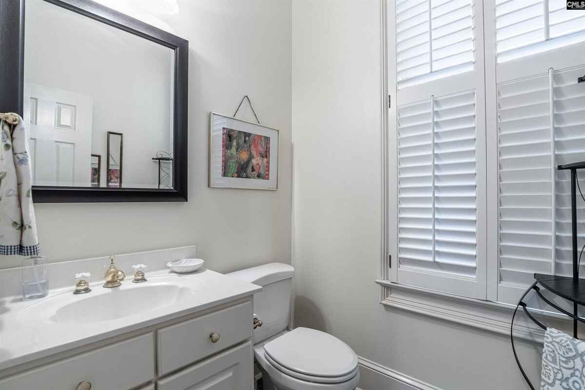 Powder room features a simple white vanity, a framed mirror, and plantation shutters.