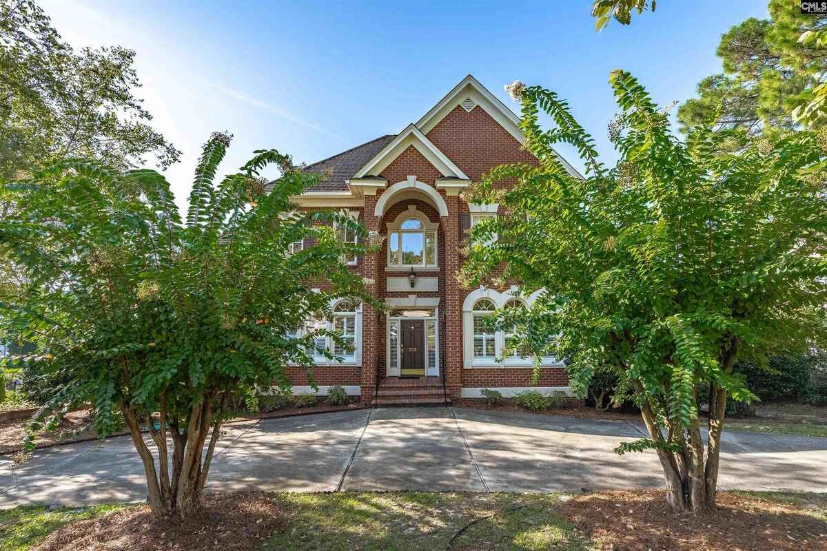 Front view of a red brick house with large arched windows framed by trees.