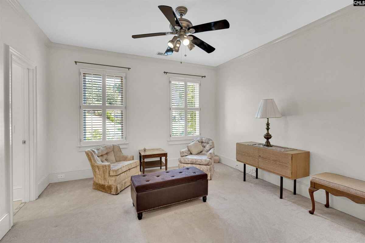 Dining area with a rectangular wooden table, surrounded by tall windows and plantation shutters.