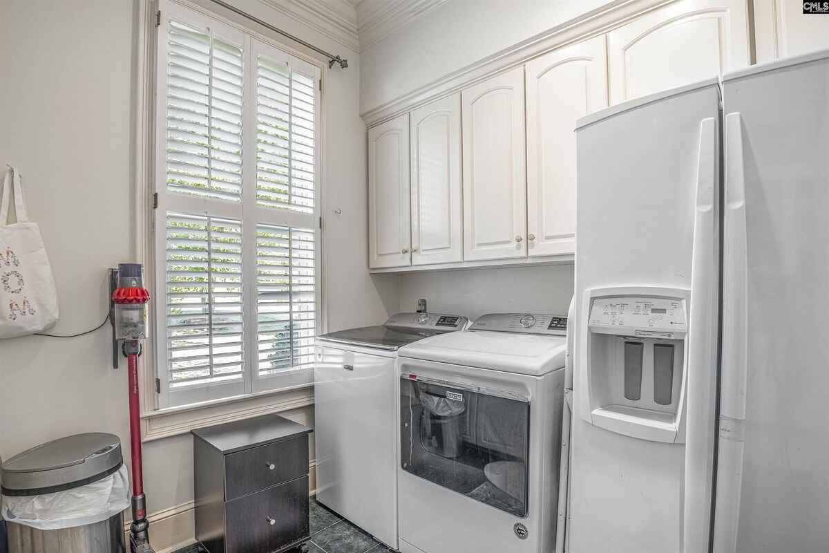 Laundry room equipped with a washer, dryer, and storage cabinets beneath a large window.