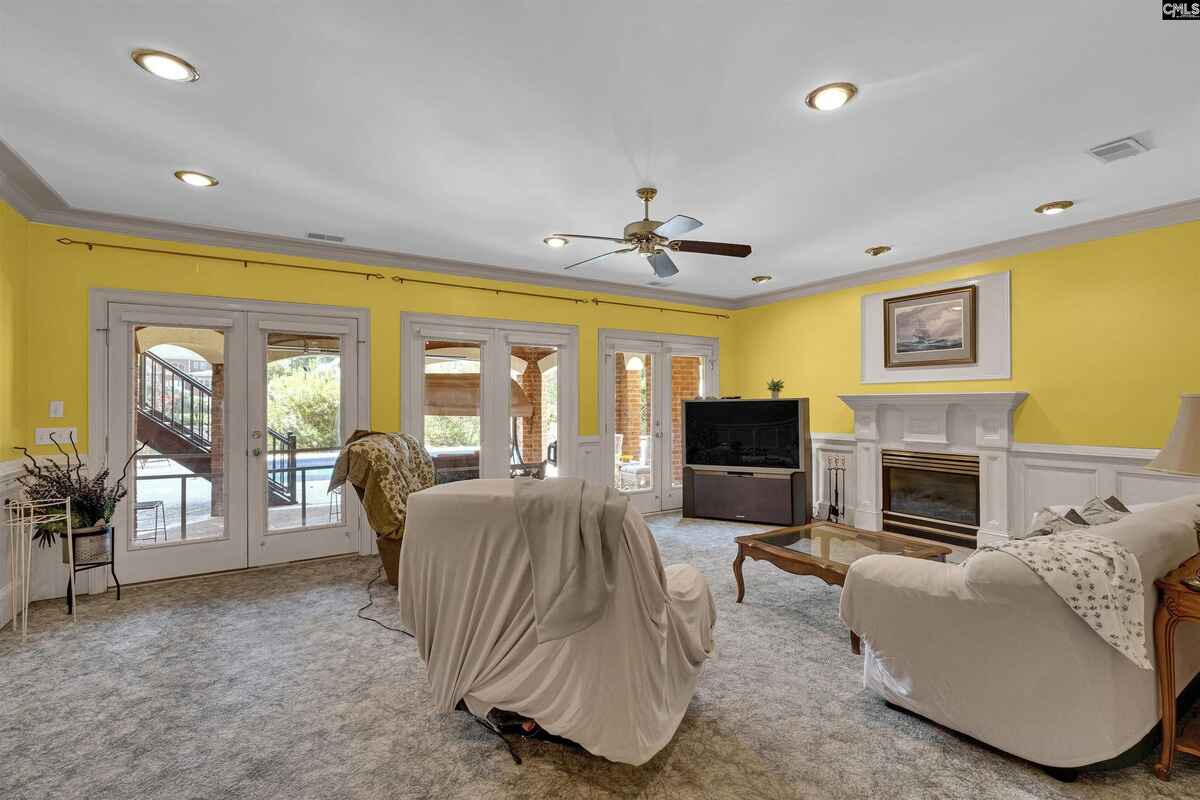 Room features yellow walls, French doors leading to a patio and pool area, a fireplace, and furniture including a covered recliner and sofa.