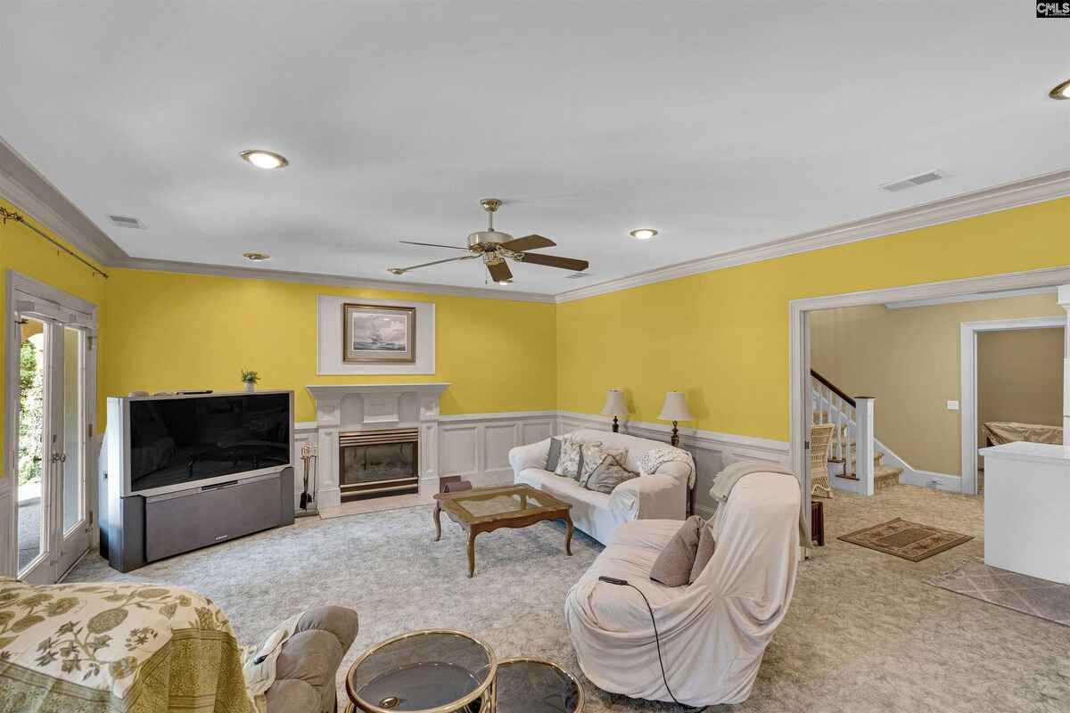 Living room features yellow walls, a fireplace, a television, and furniture including a sofa and covered recliner, with French doors opening to an outdoor area.