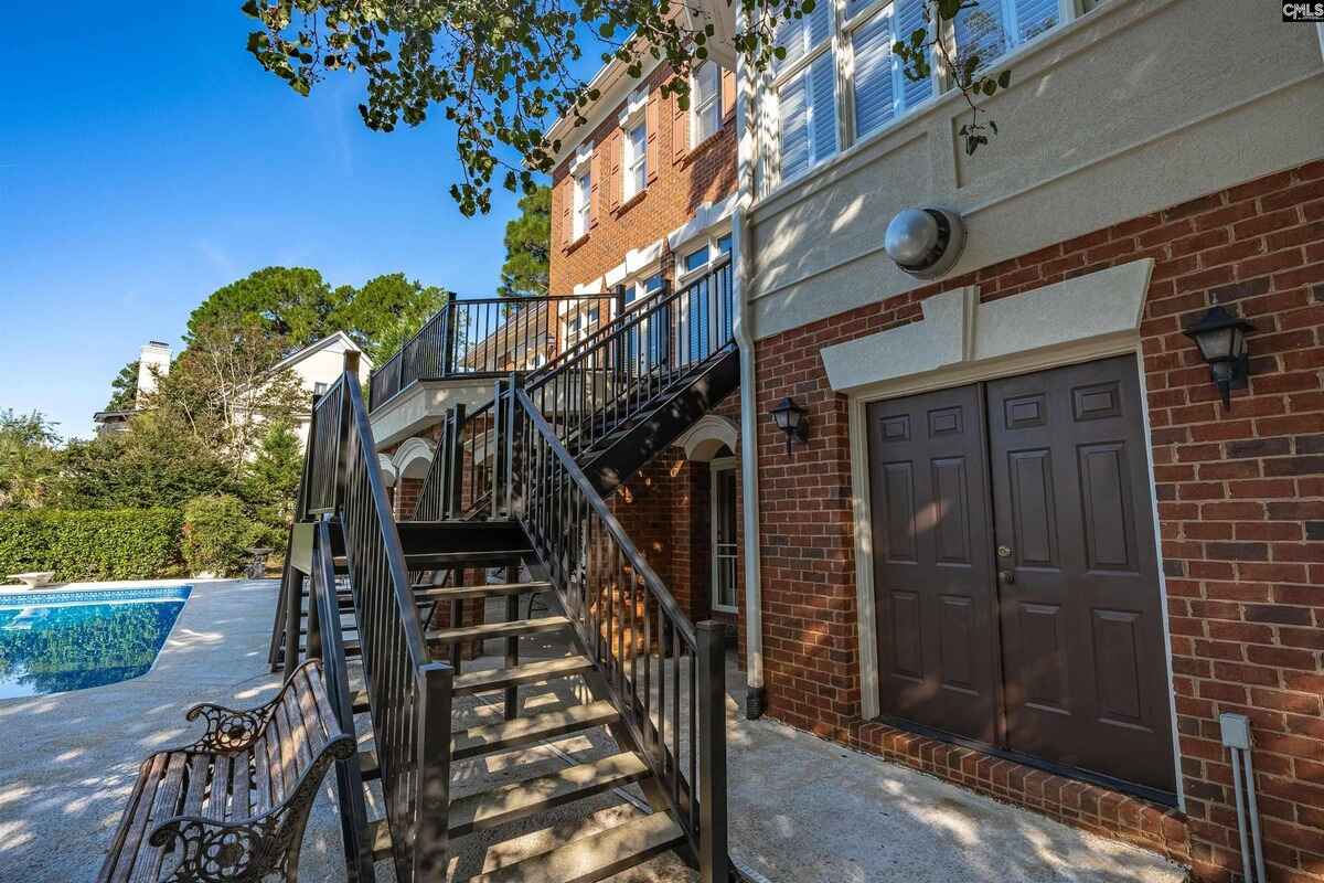 Exterior stairs lead to a patio area surrounded by brick and landscaping.