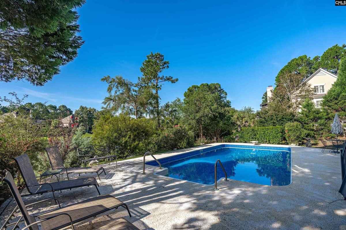 Pool area is surrounded by greenery and includes lounge chairs for relaxation.