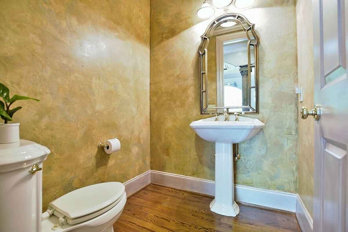 Powder room features a pedestal sink, decorative mirror, and textured walls.