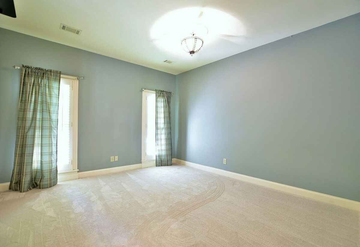 Secondary bedroom features soft carpeting, light blue walls, and natural light from two windows.