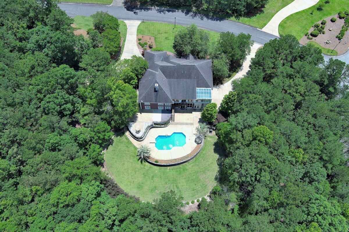 Aerial view showcases the property surrounded by lush greenery and a circular driveway.