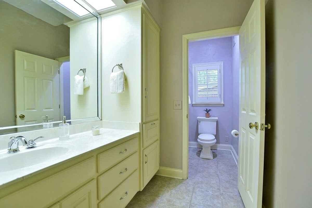 Bathroom offers a dual-sink vanity, tiled flooring, and a private toilet area with a window.