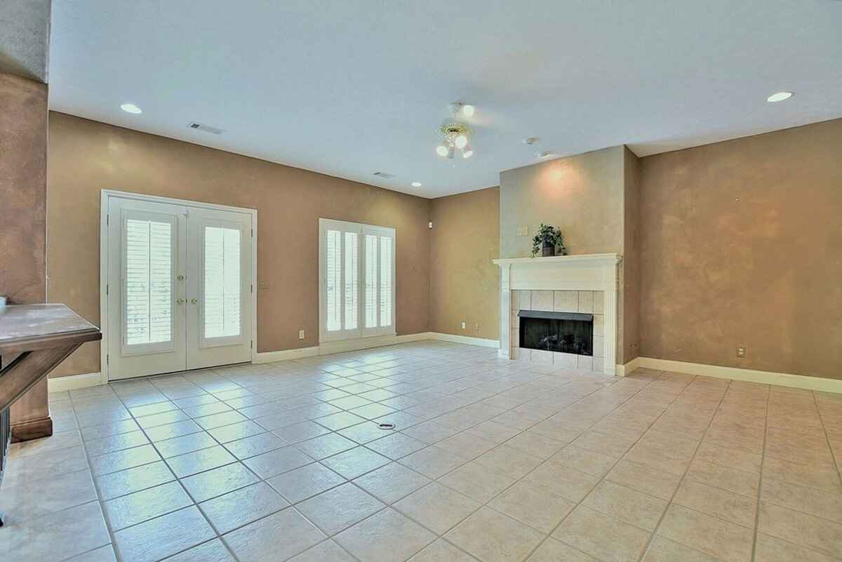 Spacious tiled living room features French doors and a fireplace with a neutral color palette.