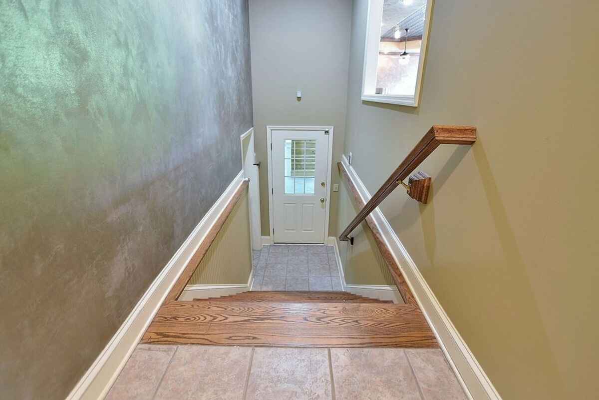 Stairway includes a wooden handrail and leads to a lower-level entry with a tiled landing.