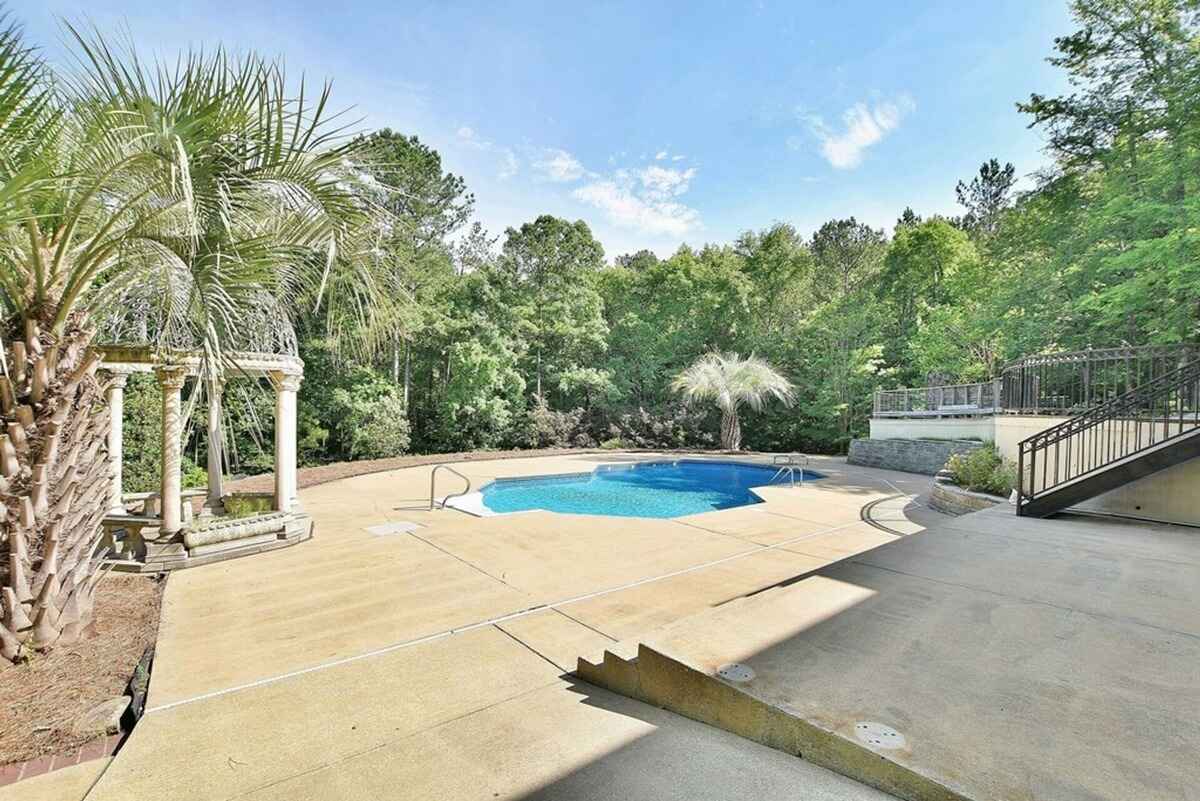 Outdoor pool area is surrounded by lush greenery and includes decorative pillars and a concrete deck.