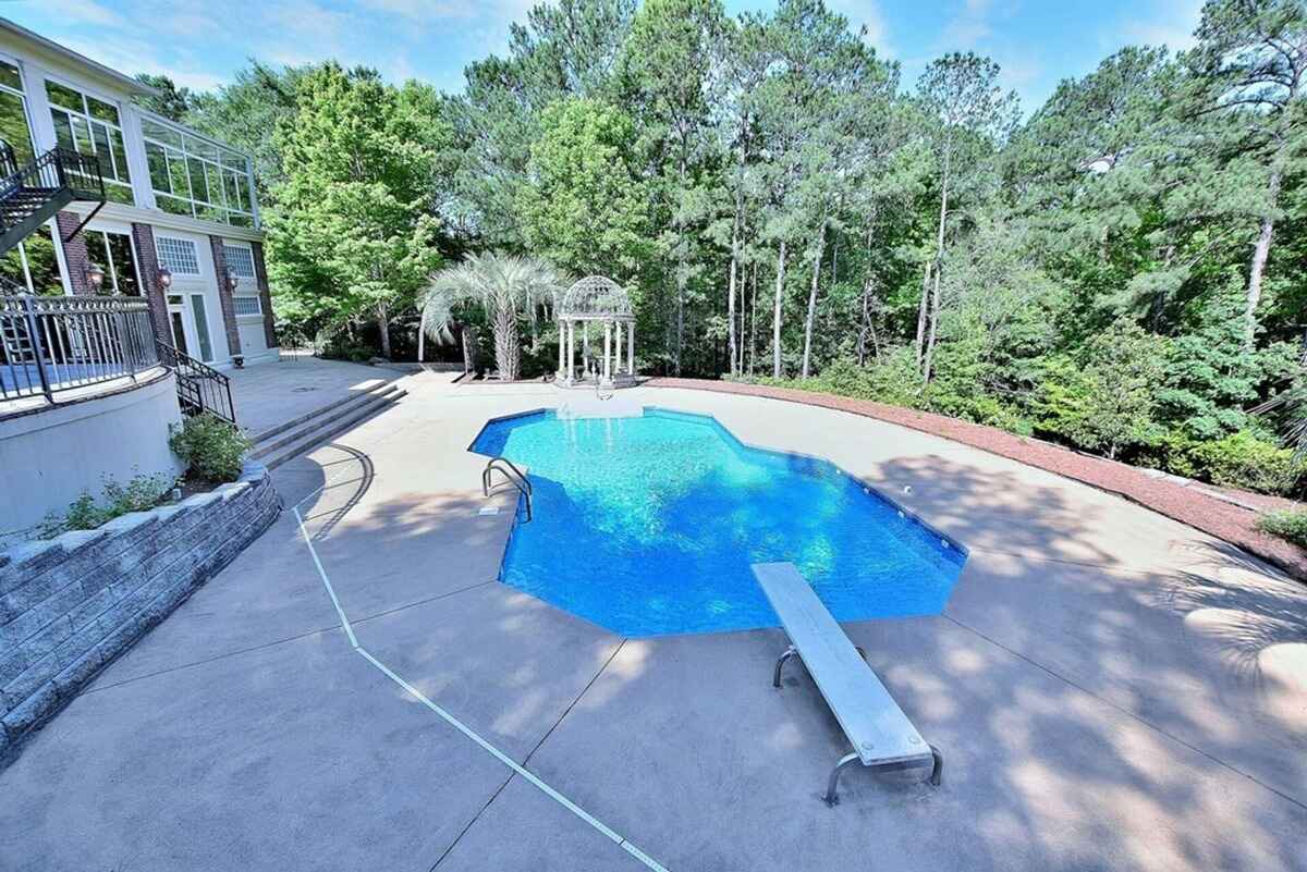 Large in-ground pool with a diving board sits in a landscaped yard featuring a gazebo.