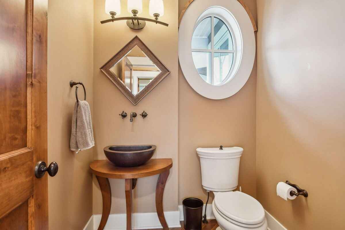 Powder room includes a round window, vessel sink, and a wooden vanity.