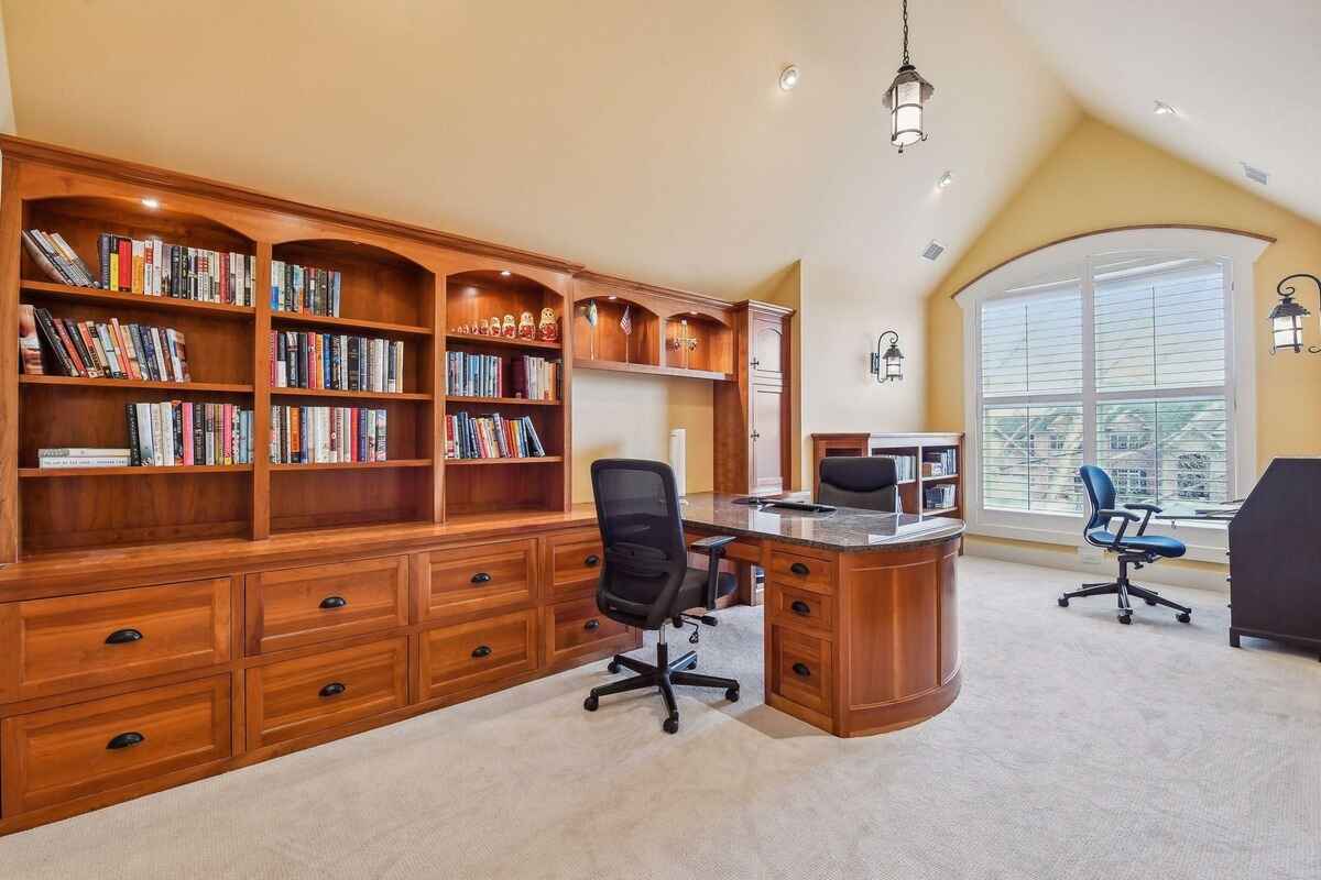 A home office is equipped with built-in wooden shelves, drawers, and desks.