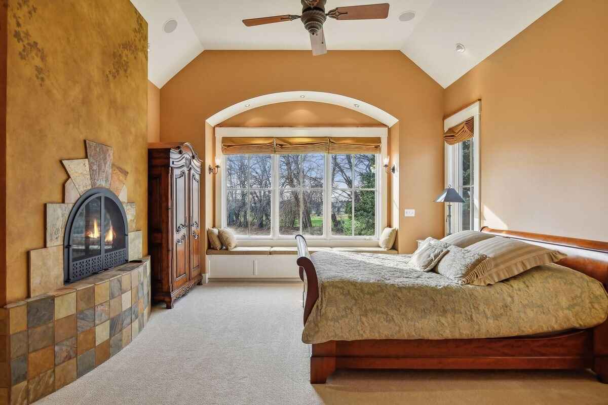 A bedroom showcases a fireplace, arched windows, and a wooden bedframe.