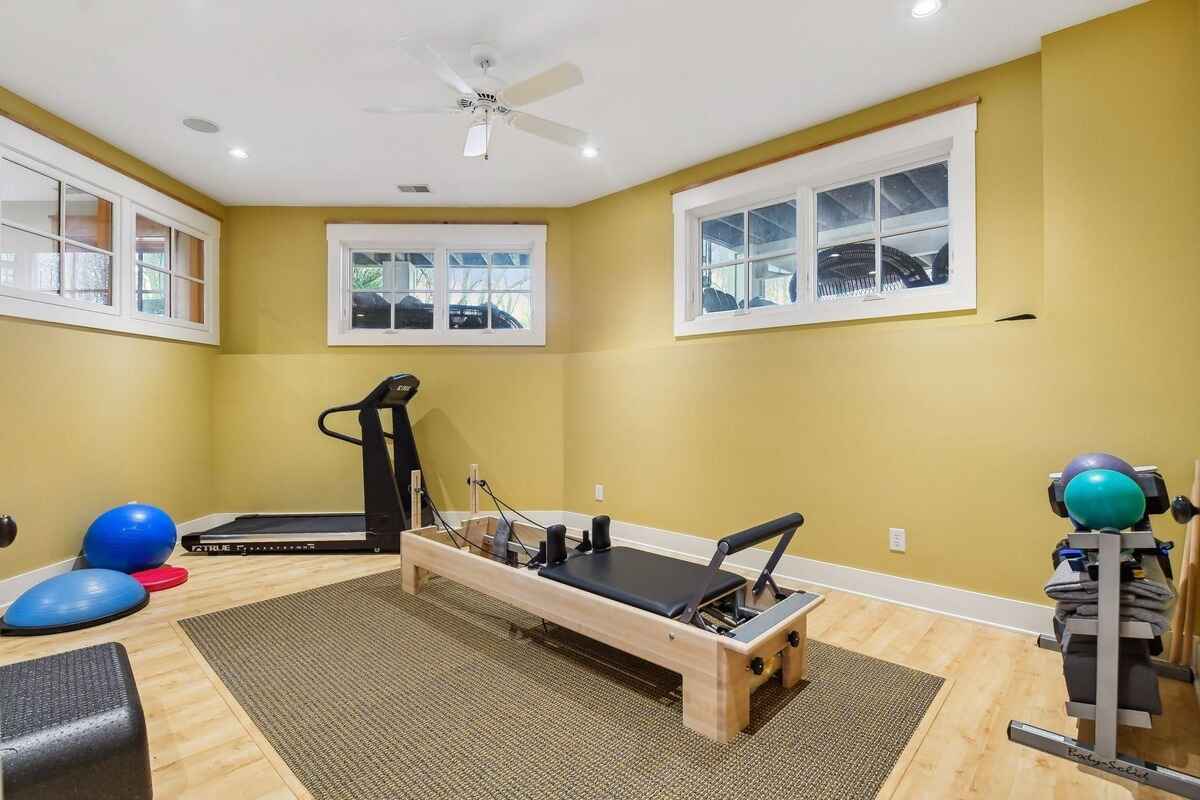 A home gym with a treadmill, Pilates reformer, and various exercise equipment is shown.