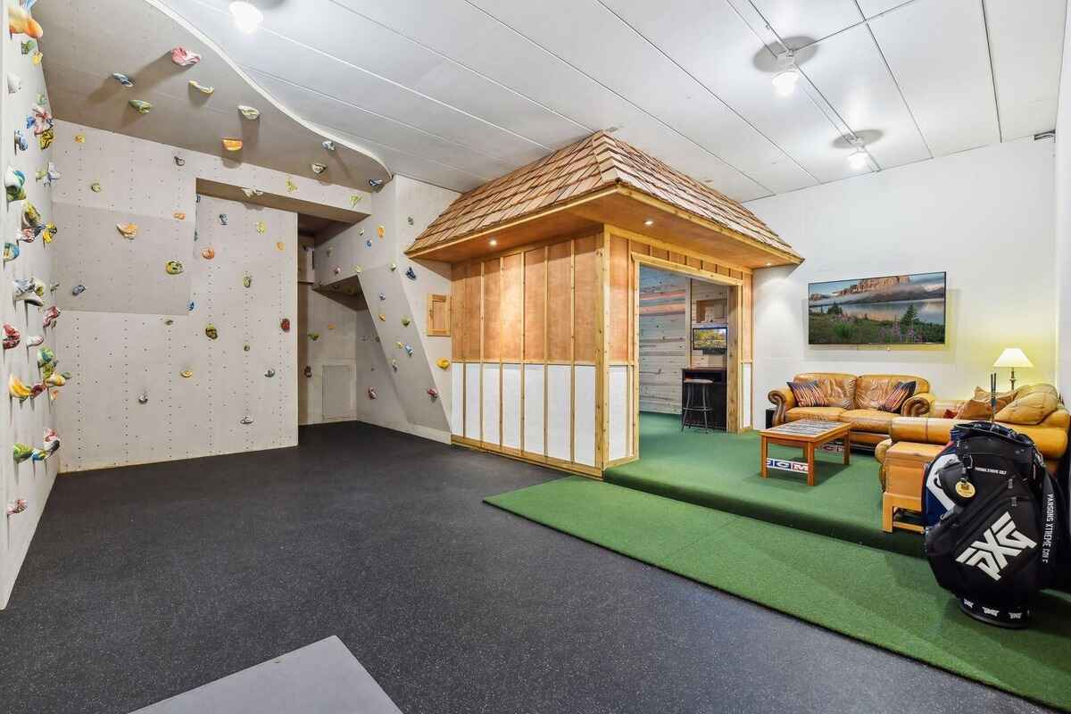 A home recreation area features a climbing wall and a small, wood-paneled room with a seating area and a putting green.