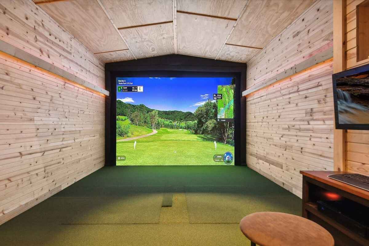 Indoor golf simulator with a large screen displaying a golf course and wood-paneled walls.