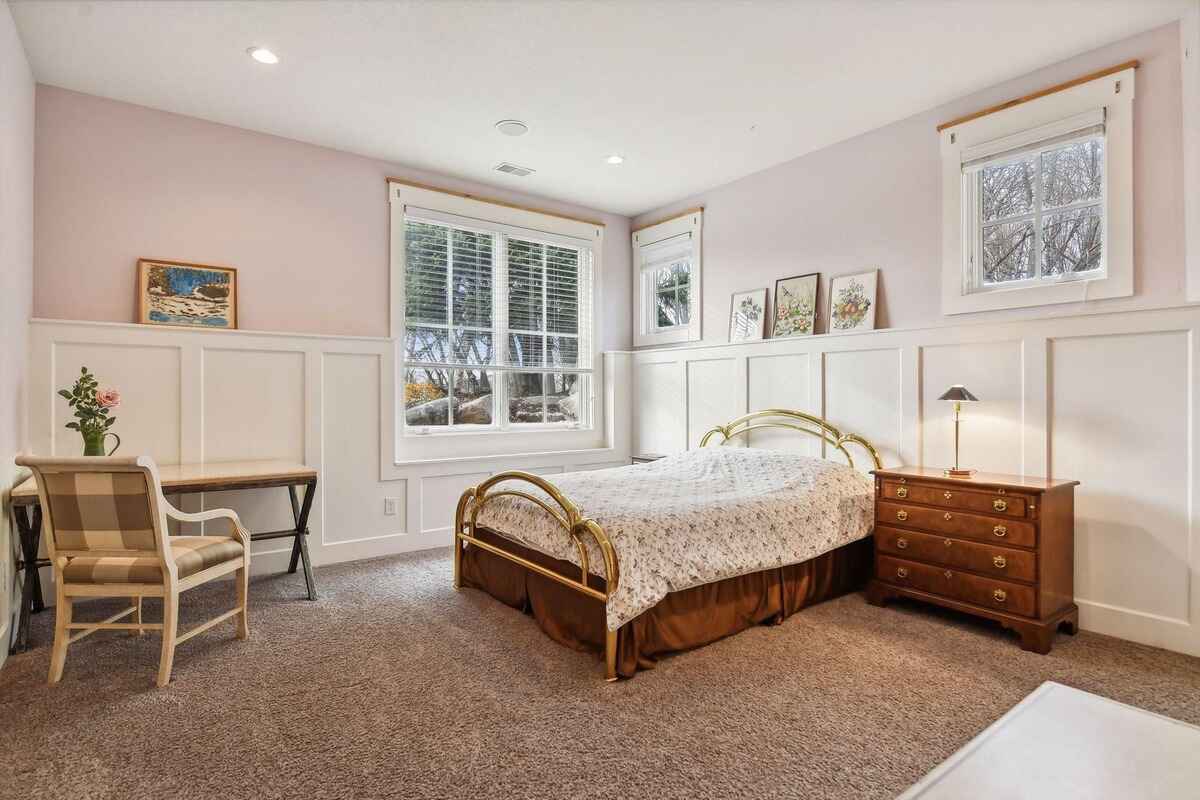 A bedroom with light pink walls, white wainscoting, and a brass bed frame is shown.