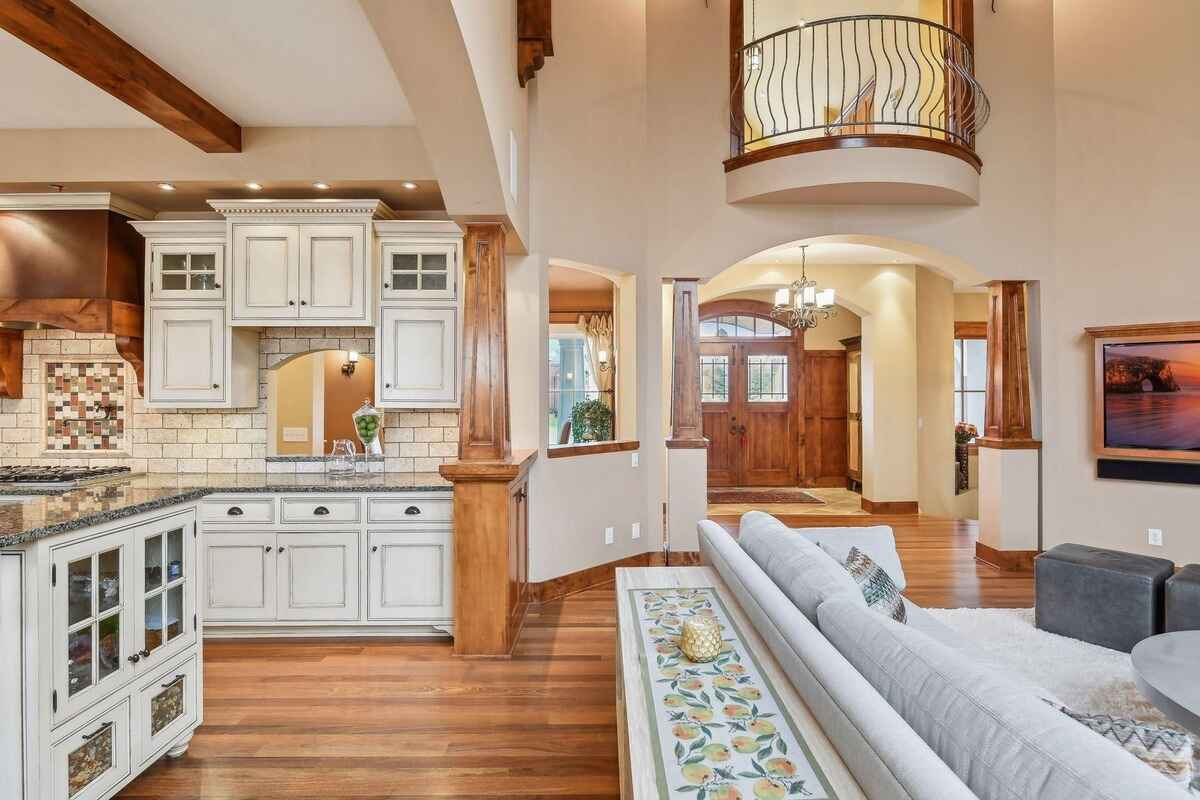 The kitchen includes a large island with pendant lights, white cabinetry, and wooden beams.