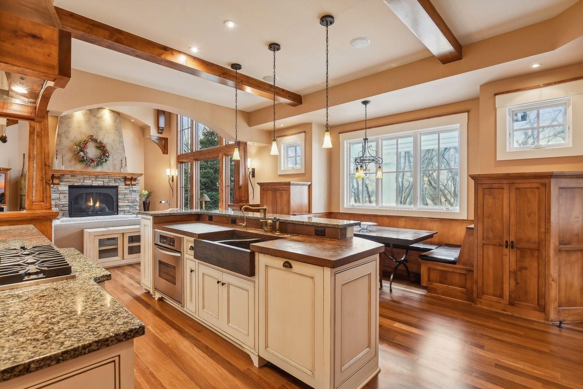 The dining nook features a built-in wooden bench, large windows, and a chandelier.