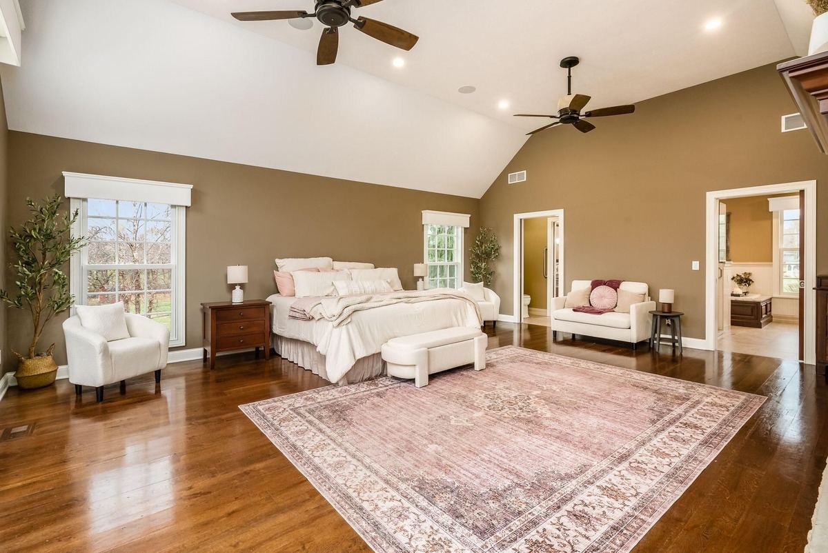 Large bedroom with vaulted ceilings, wood floors, and neutral-toned furniture.