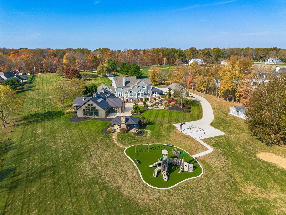 Wide-angle aerial view showing a playground, driveway, and expansive lawns on the property.