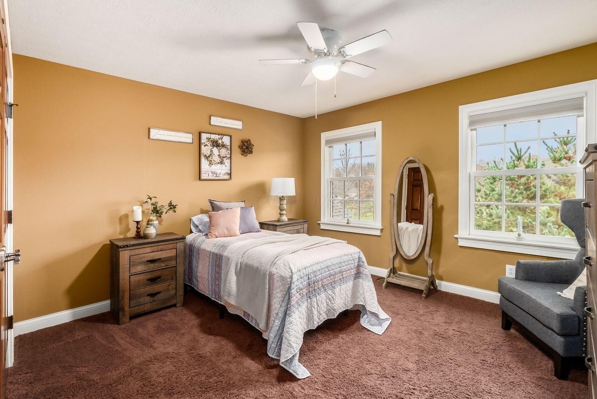 Bedroom with yellow walls, twin bed, and large windows for natural light.