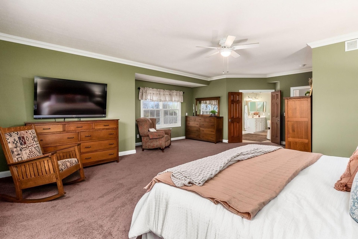 Large bedroom with green walls, carpet flooring, and an attached seating area.