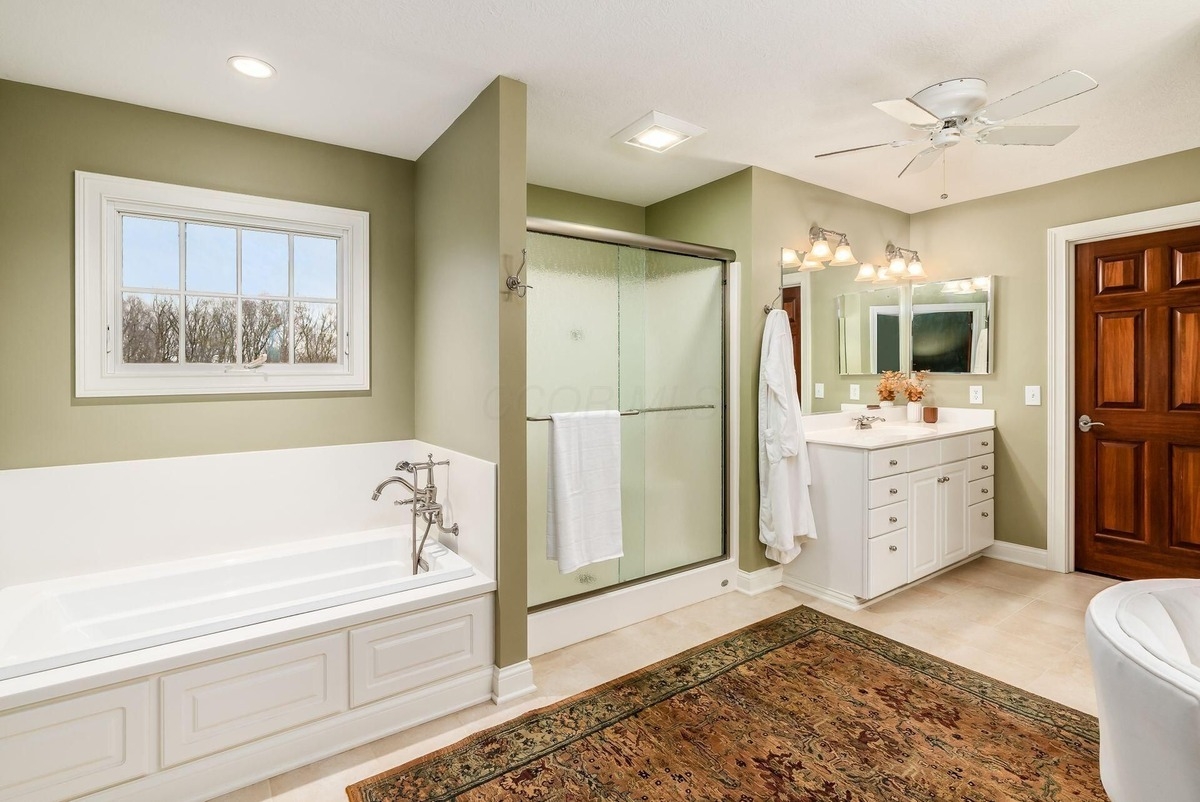 Bathroom with a soaking tub, glass-enclosed shower, and dual sinks.